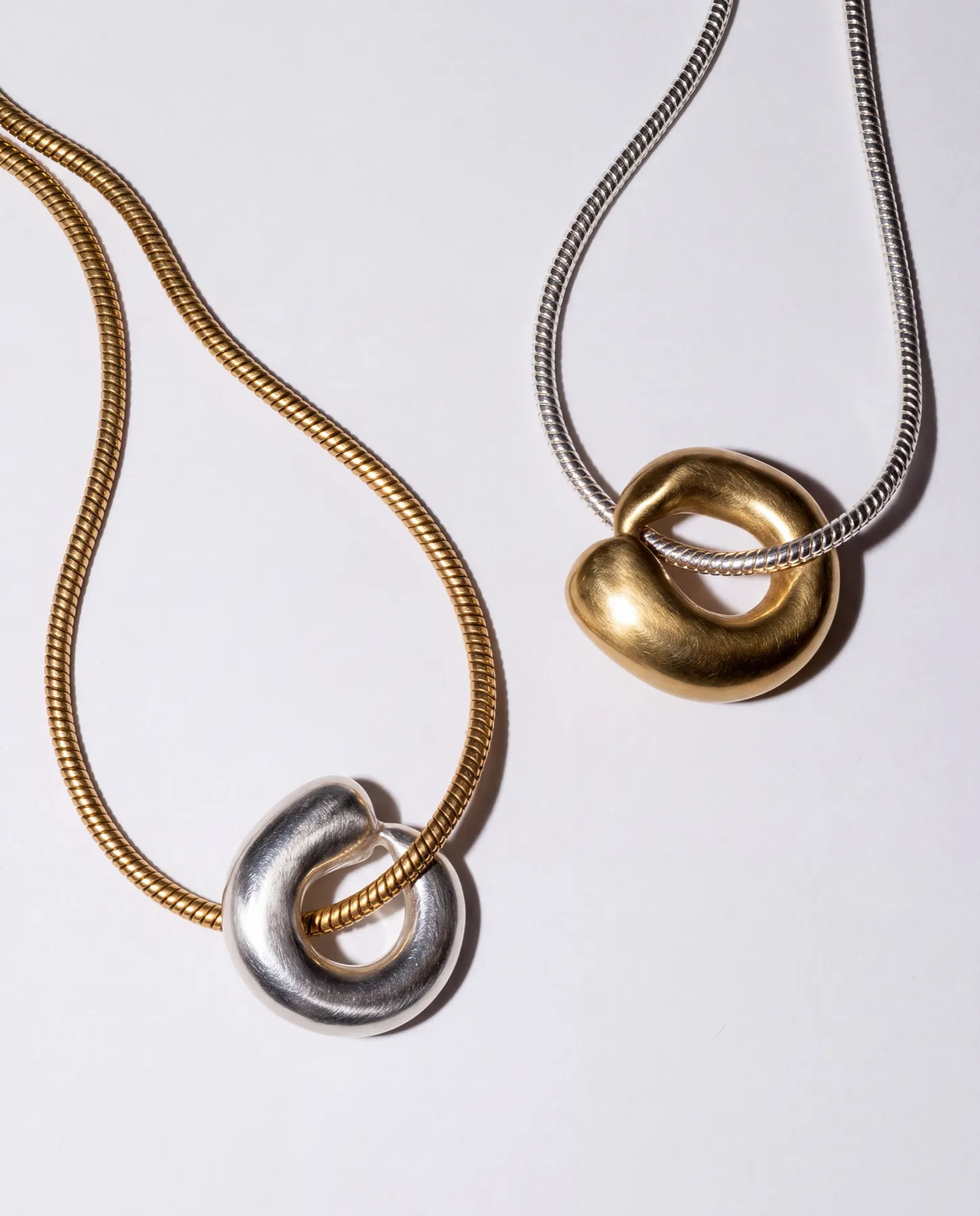 Gold and silver snake chains with sculpted pendants on a pale surface