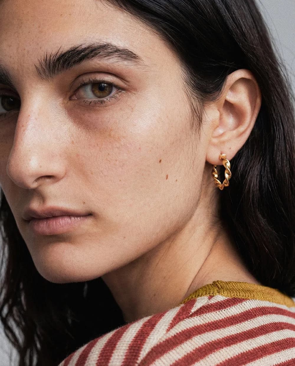 Extreme close-up of a model's face and twisted gold hoop earring