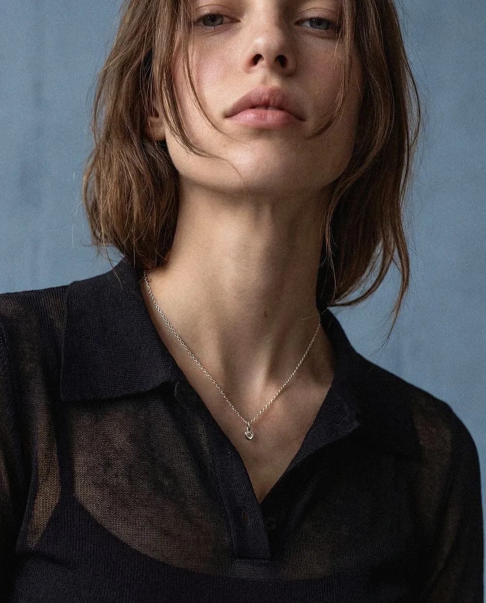 Model in a sheer black shirt wearing a fine silver necklace