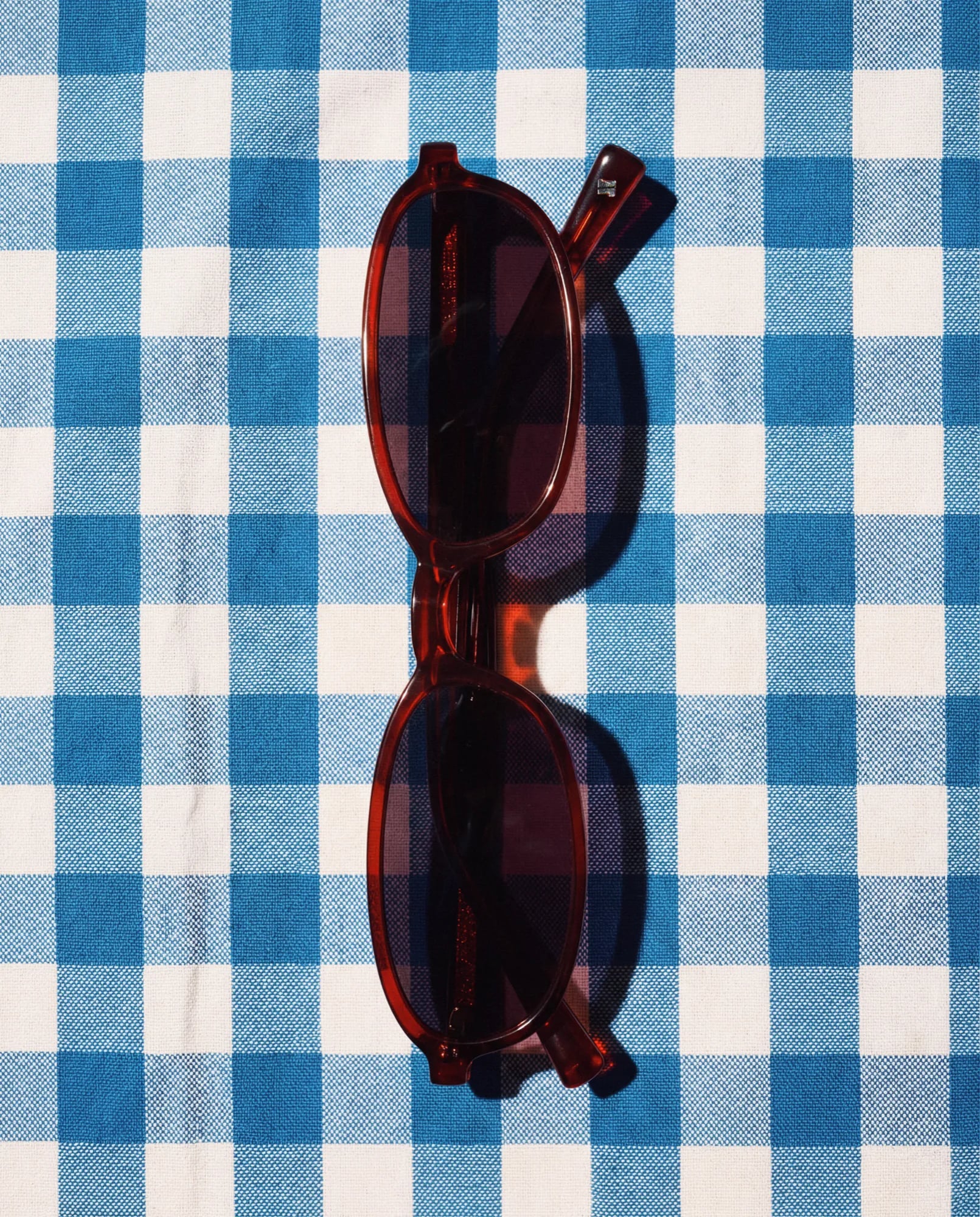 Lunettes de soleil en acétate bordeaux sur une nappe vichy bleue et blanche