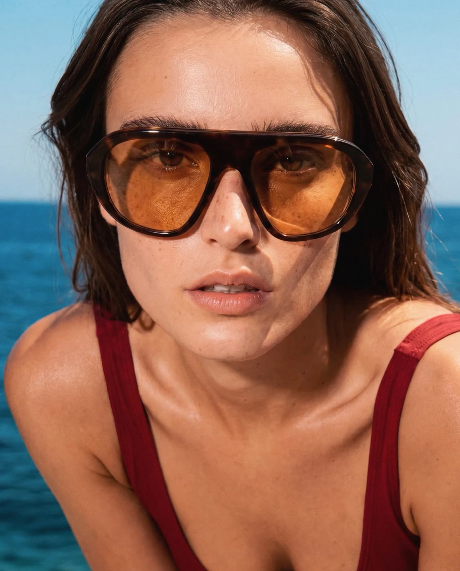 Model in tortoiseshell sunglasses with amber lenses and a red swimsuit, by the sea