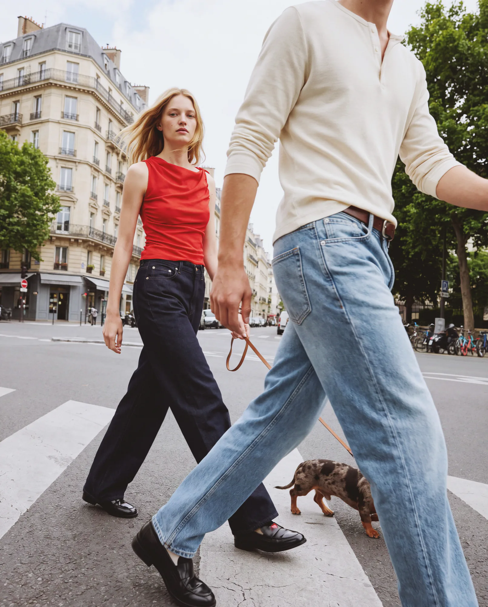 Two models in jeans and black loafers crossing a Paris street with a dachshund on a lead