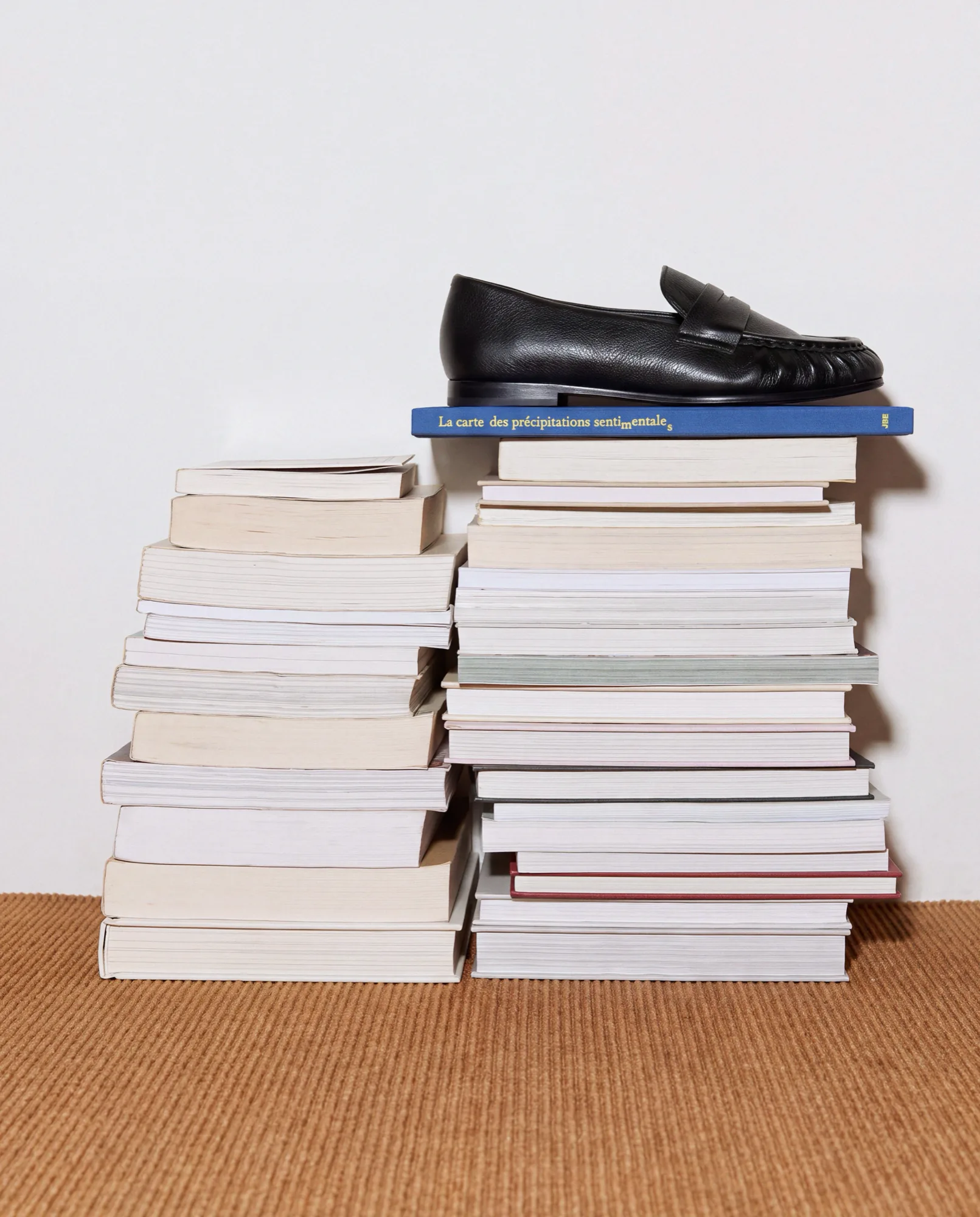 Mocassin noir posé sur une pile de livres, sur un tapis en sisal
