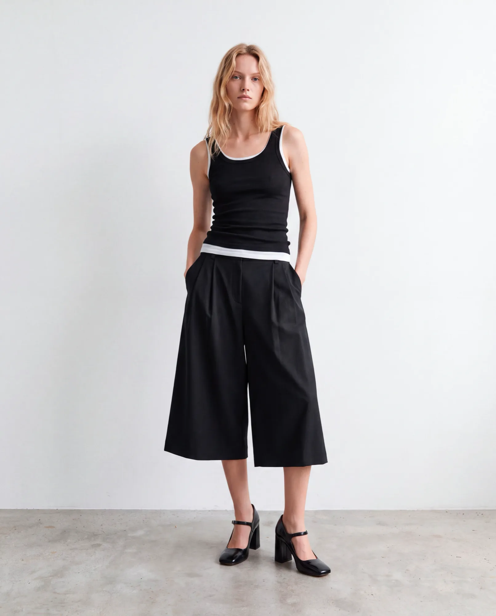 Model in a black tank top, black culottes and Mary Jane heels