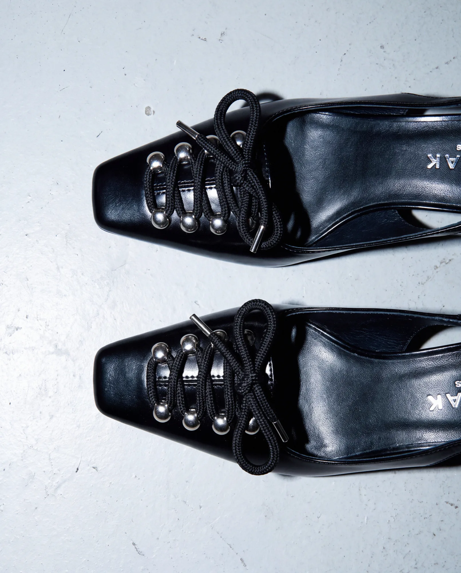 Black patent lace-up shoes with eyelets on a pale blue background
