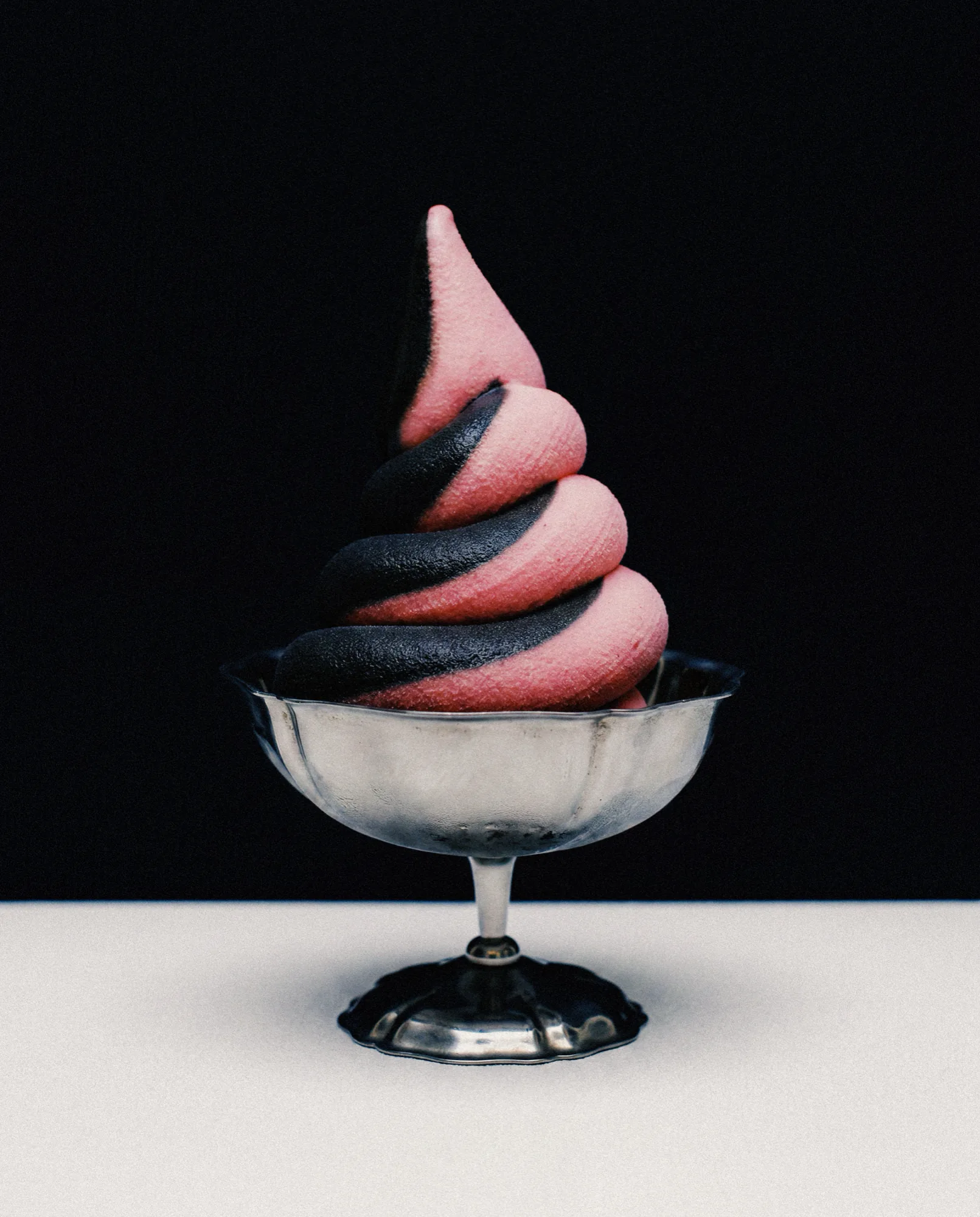 Glace à l’italienne rose et noire dans une coupe argentée, sur fond noir
