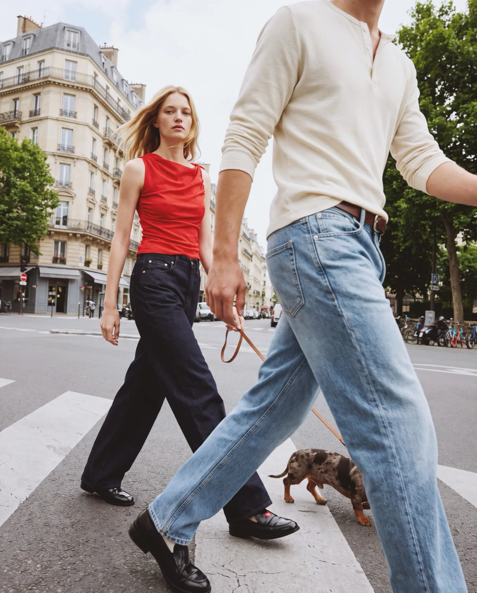 Two models in jeans and black loafers crossing a Paris street with a dachshund on a lead