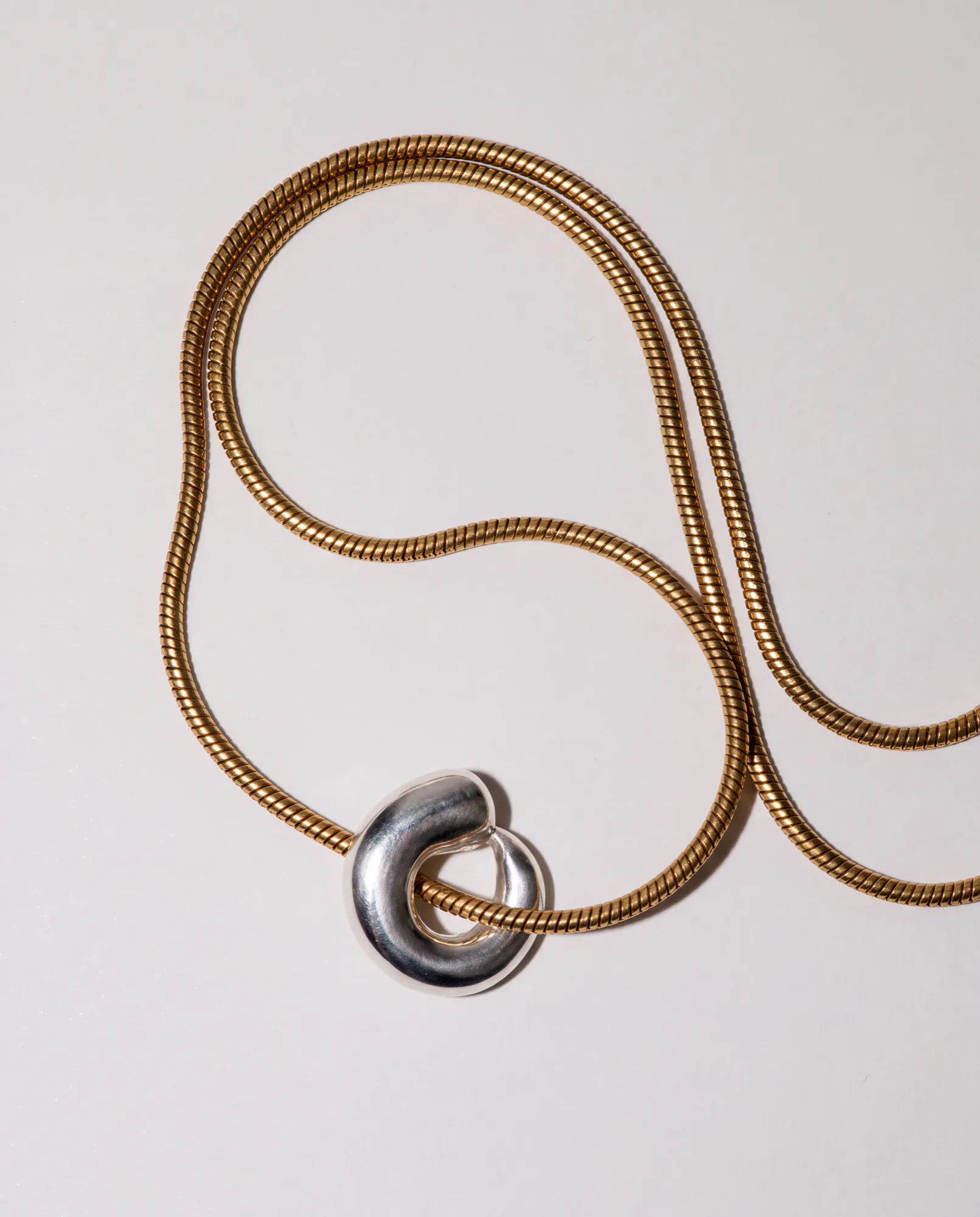 Collier maille serpent doré avec un pendentif sculpté en argent sur un fond clair