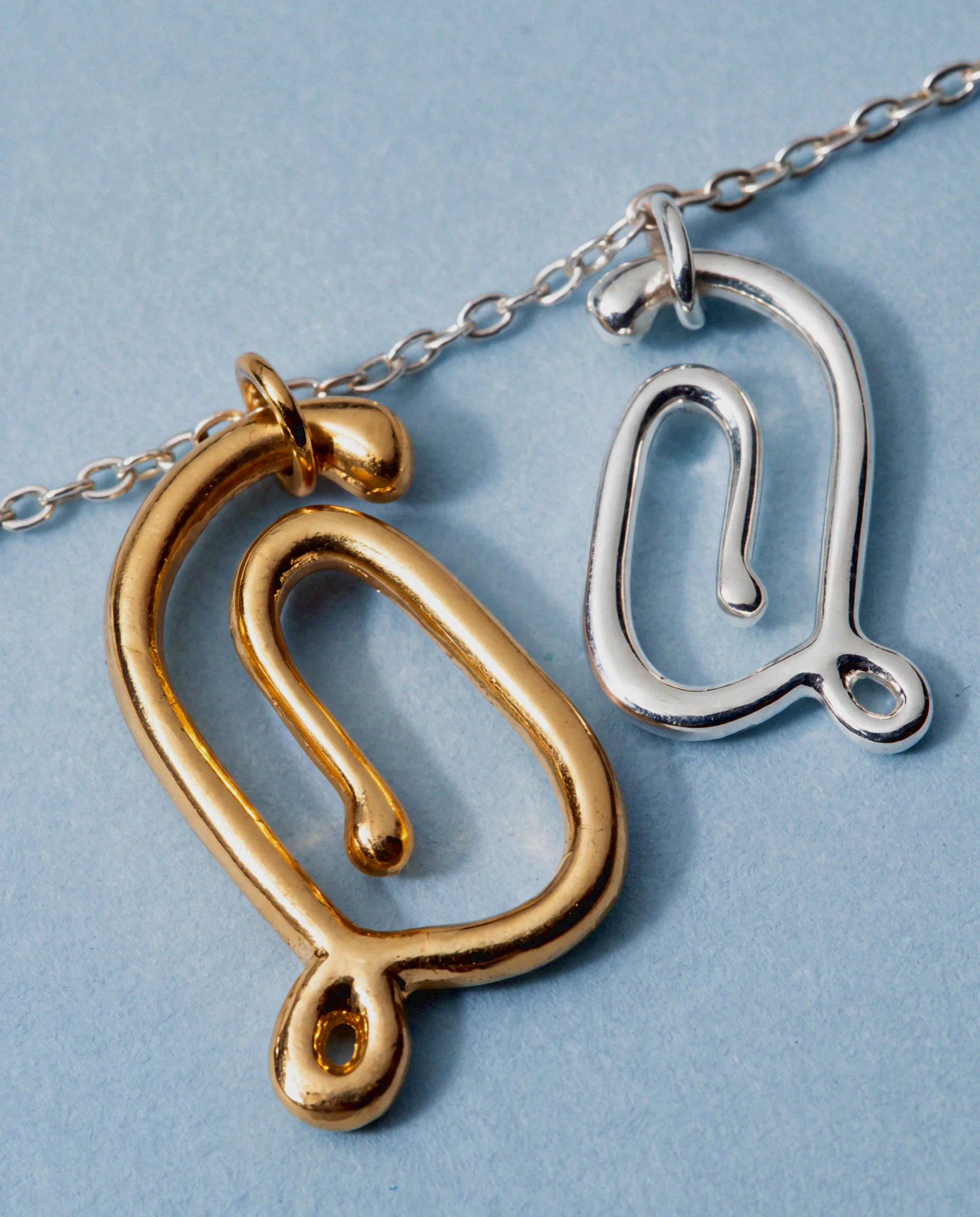 Pendentifs monogrammes dorés et argentés sur chaînes, sur fond bleu pâle