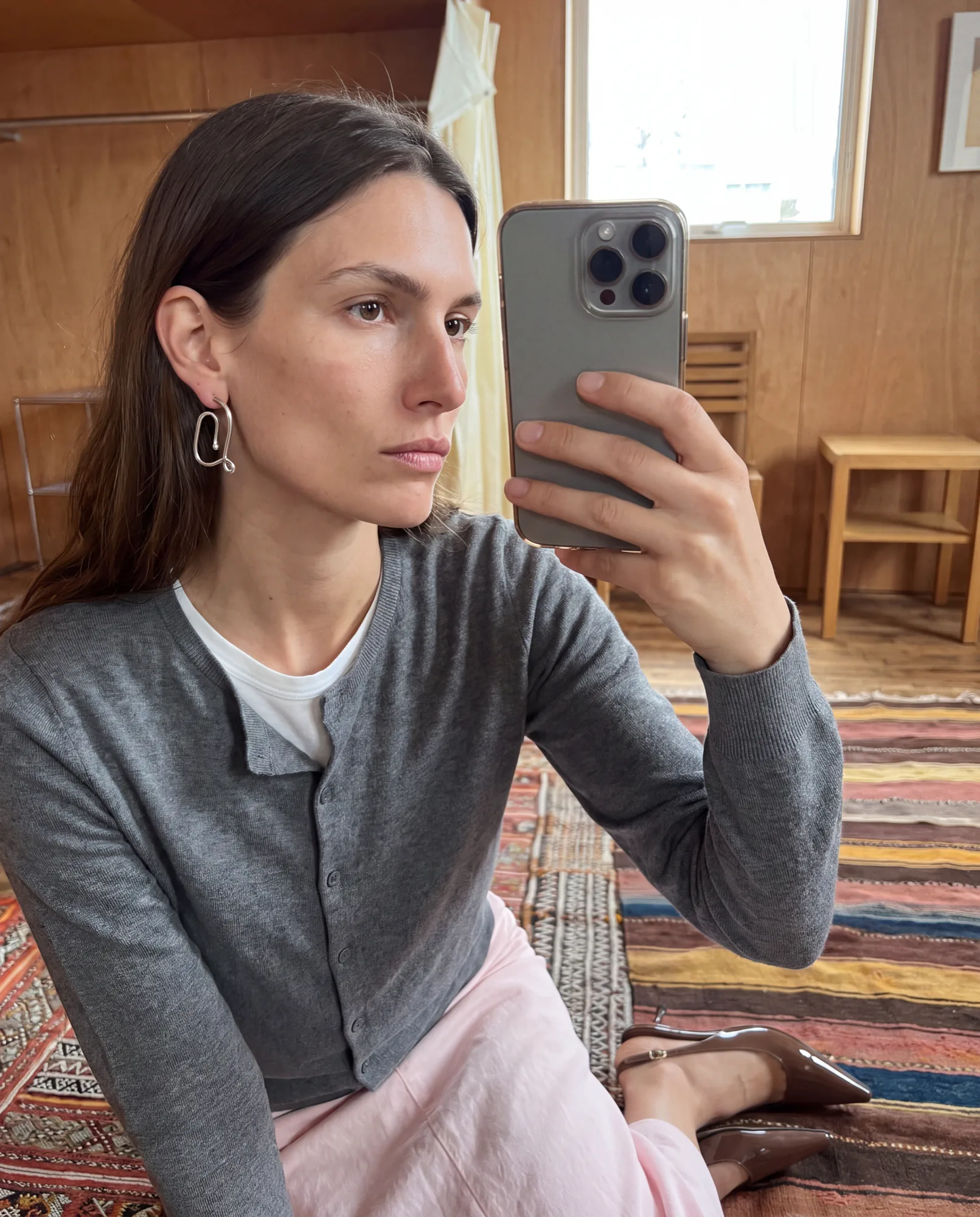 Selfie miroir d’une femme en cardigan gris portant des boucles d’oreilles pendantes, style UGC