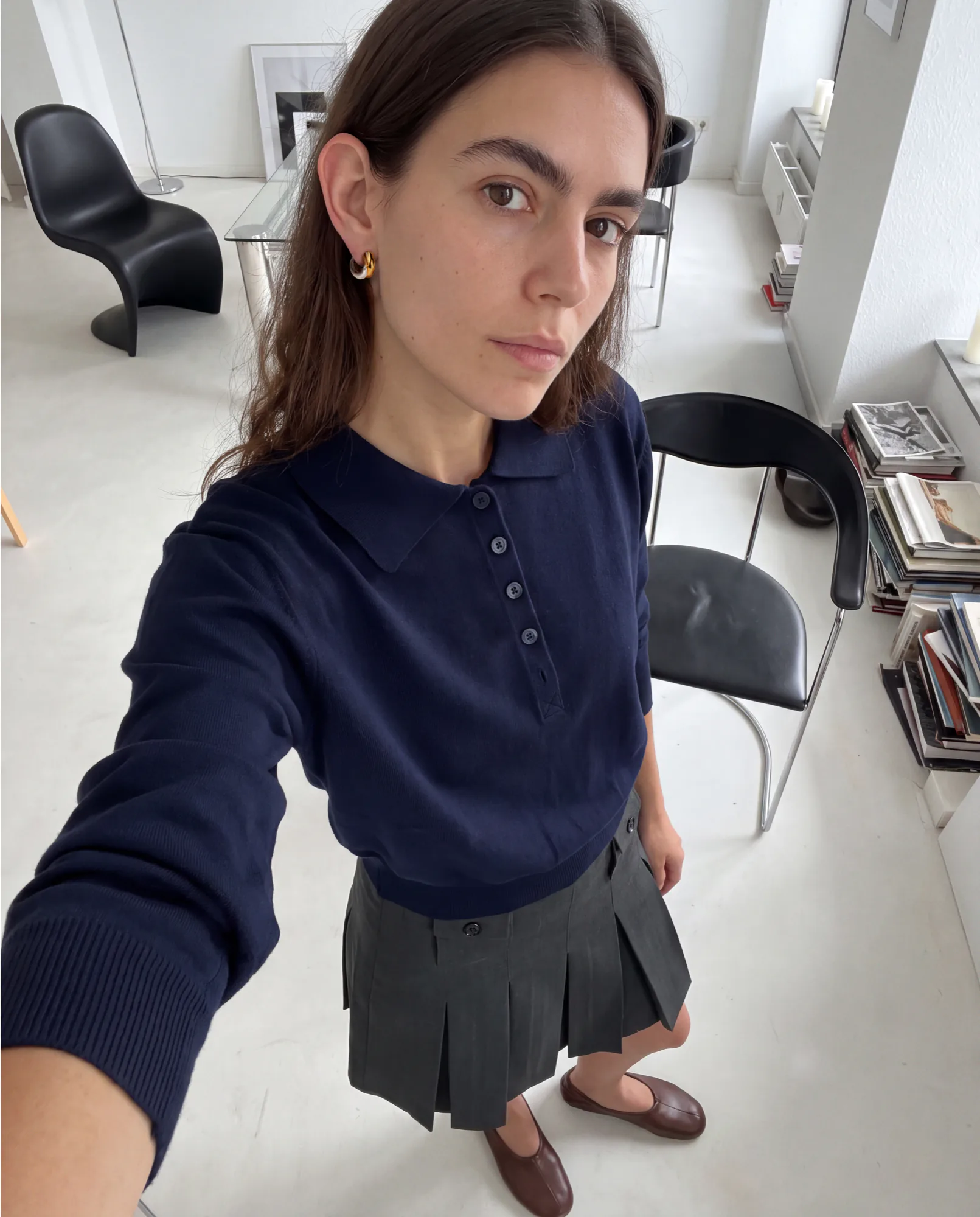 Selfie d’une femme en polo marine et jupe plissée dans un appartement lumineux, style UGC
