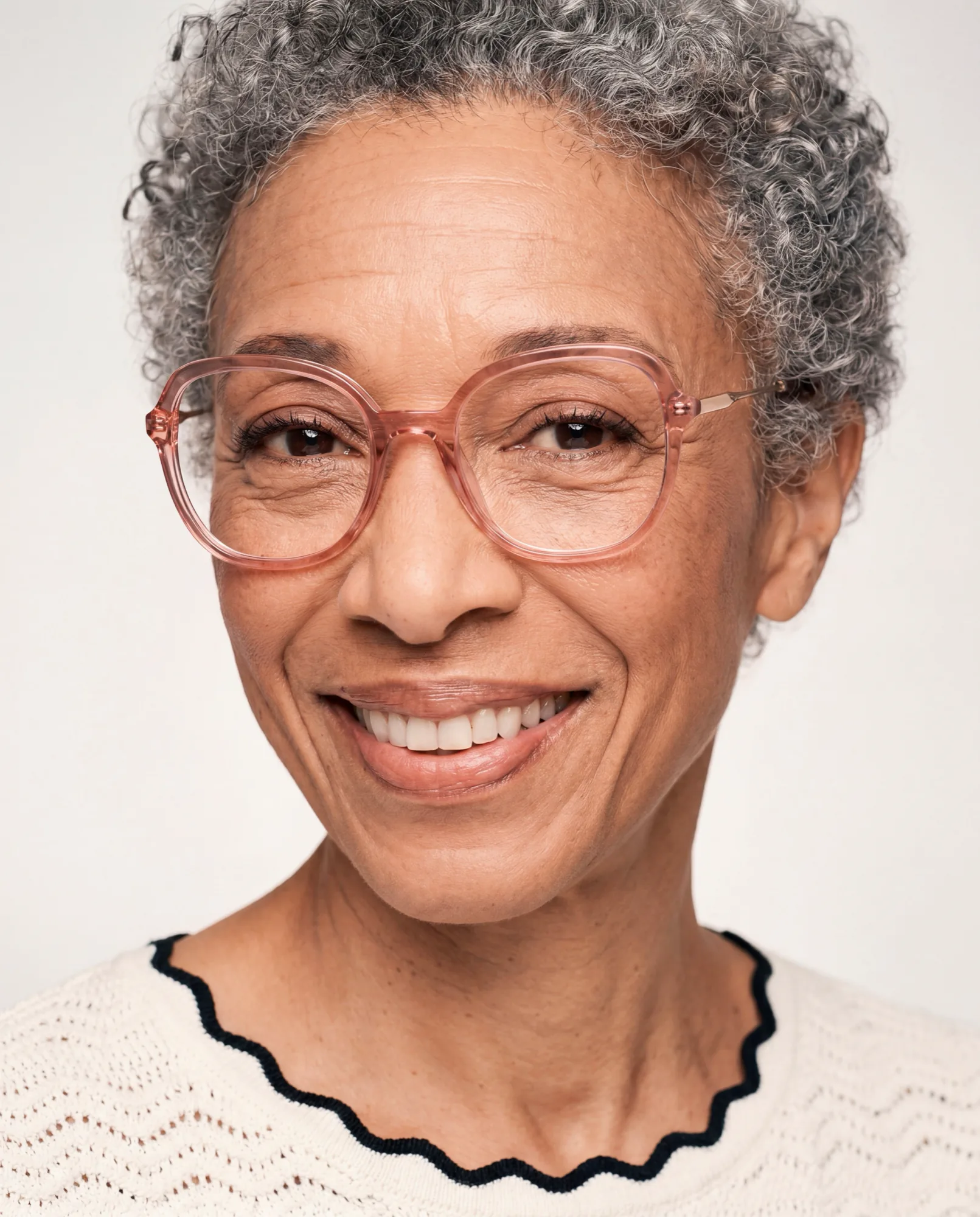 Femme souriante aux cheveux gris bouclés portant des lunettes roses translucides