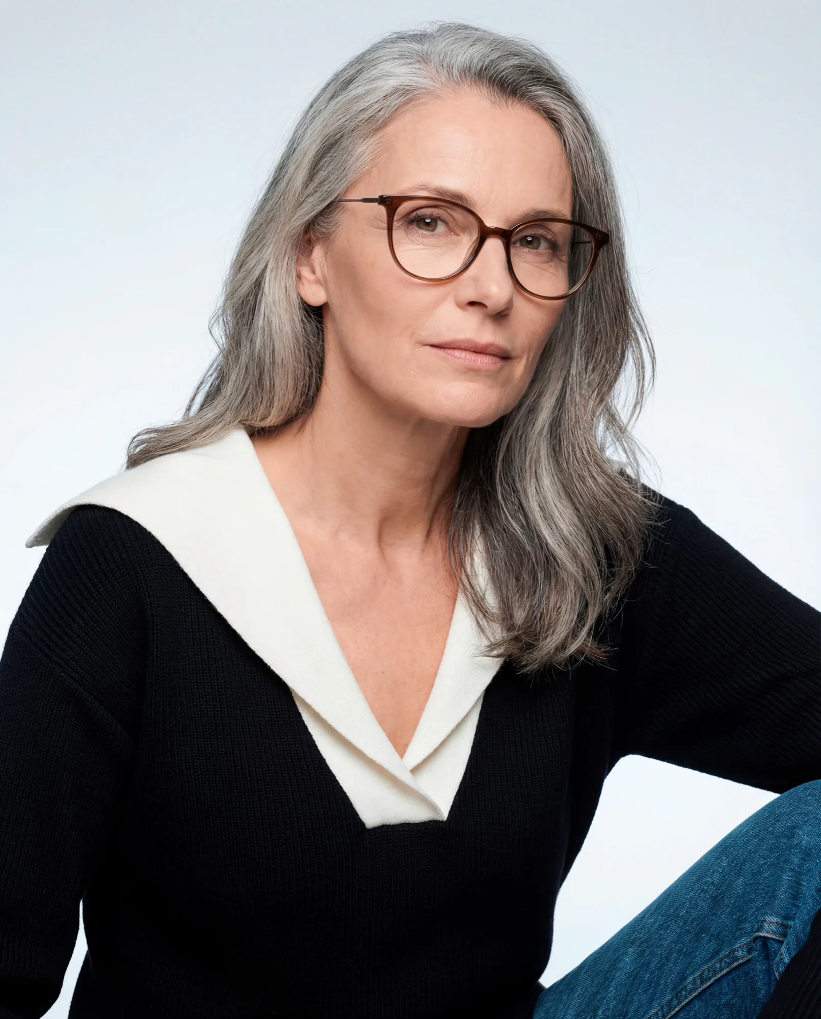 Femme aux longs cheveux gris en lunettes écaille et pull noir à col blanc