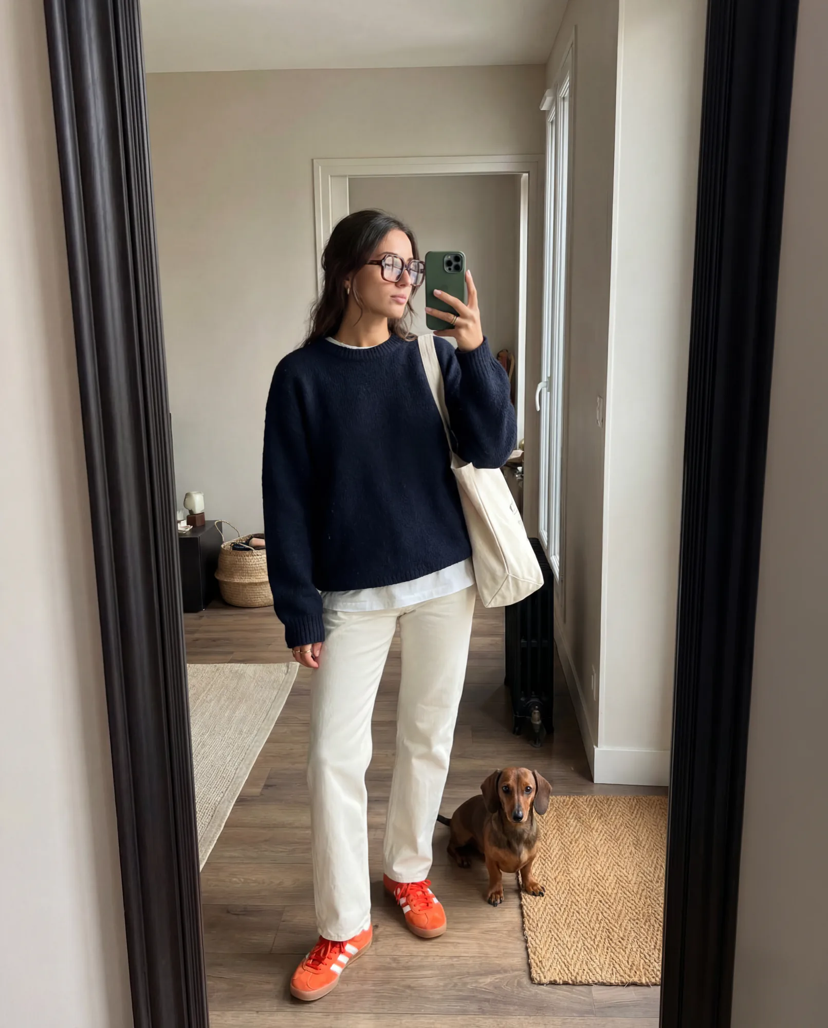 Mirror selfie of a woman in sunglasses and a navy sweater with a small dog, UGC style