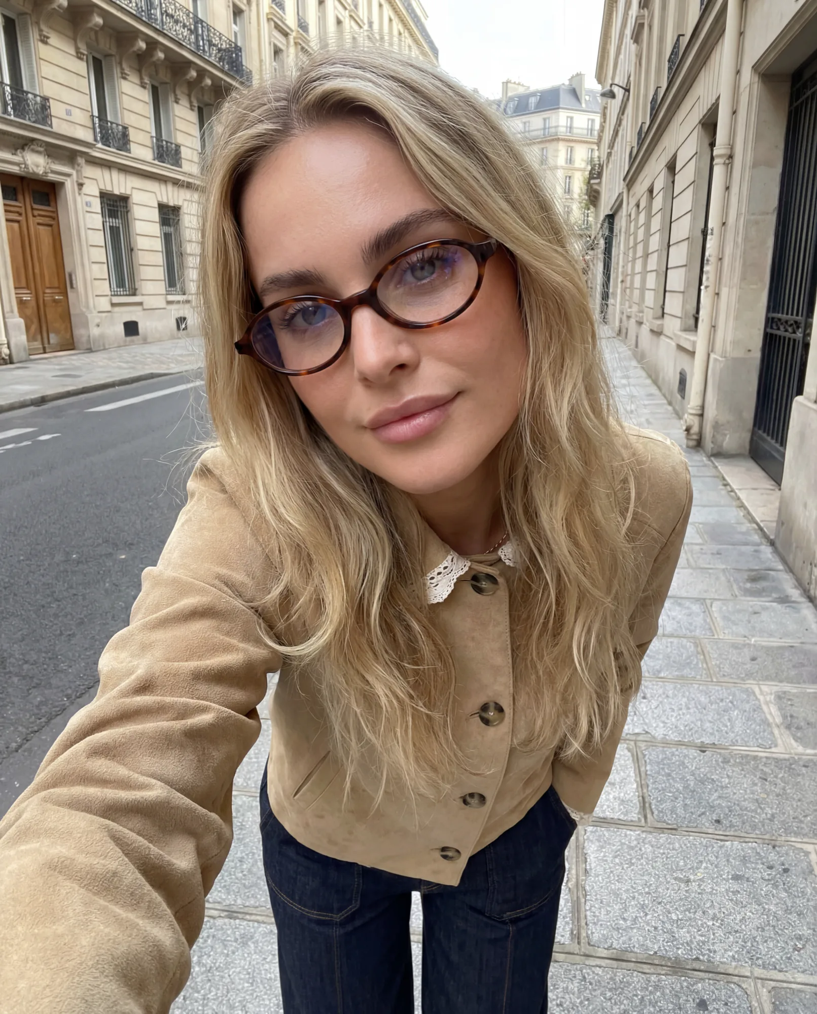 Selfie d’une femme blonde en lunettes écaille dans une rue de Paris, style UGC